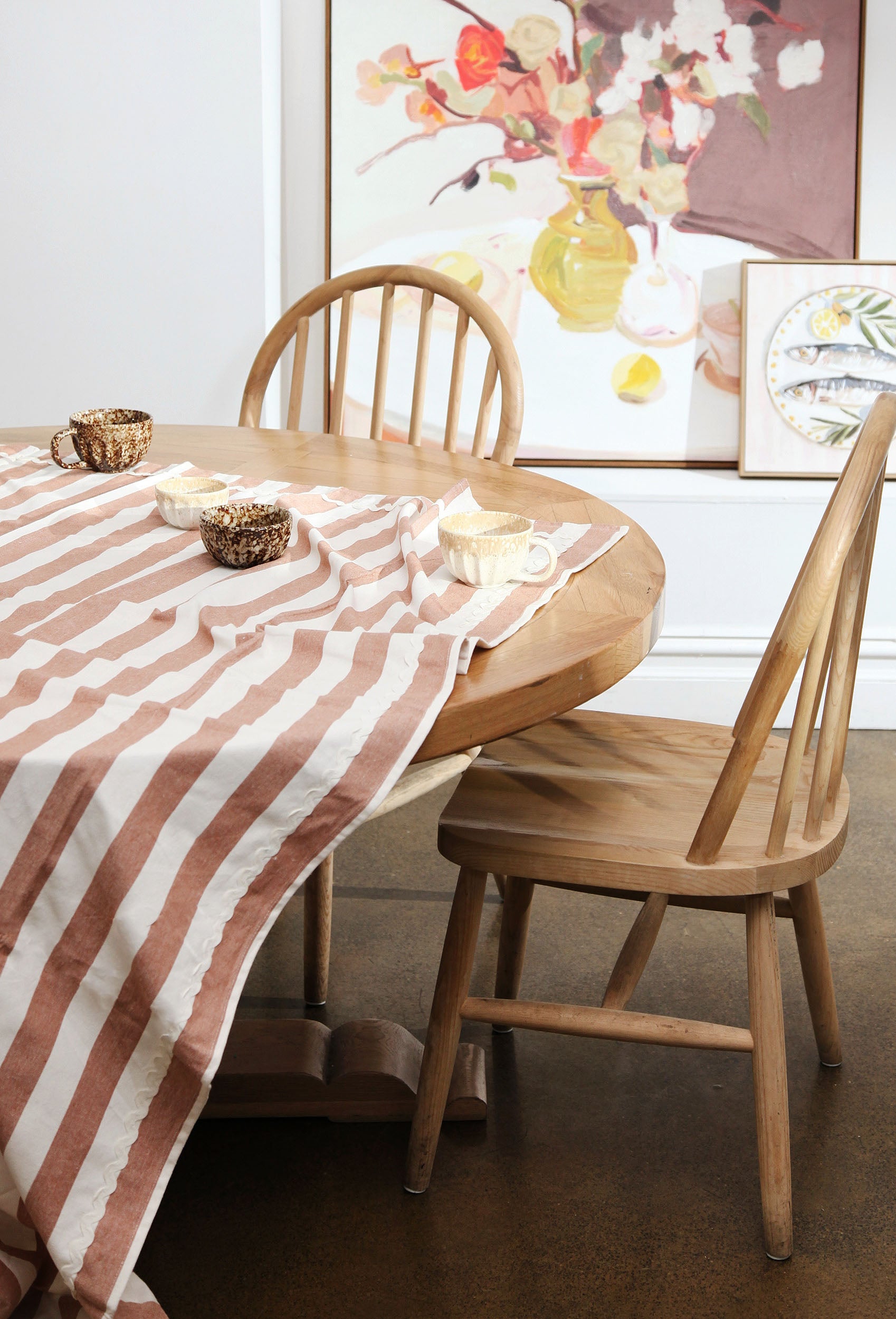 Dining table with striped tablecloth and wooden chairs in a room with framed artwork on the wall.