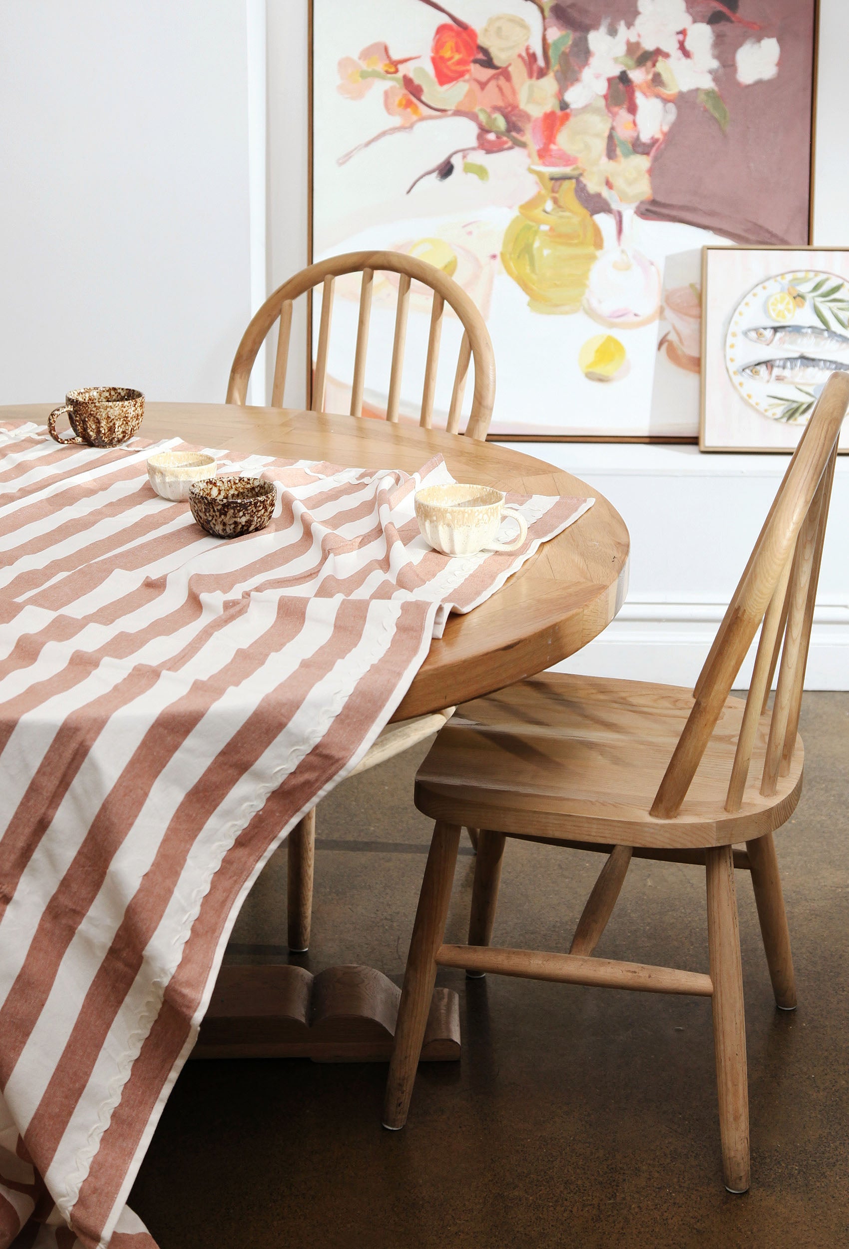 Dining table with striped tablecloth and wooden chairs in a room with framed artwork on the wall.