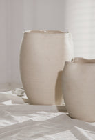Two beige ceramic pots on a white surface with a light gray background