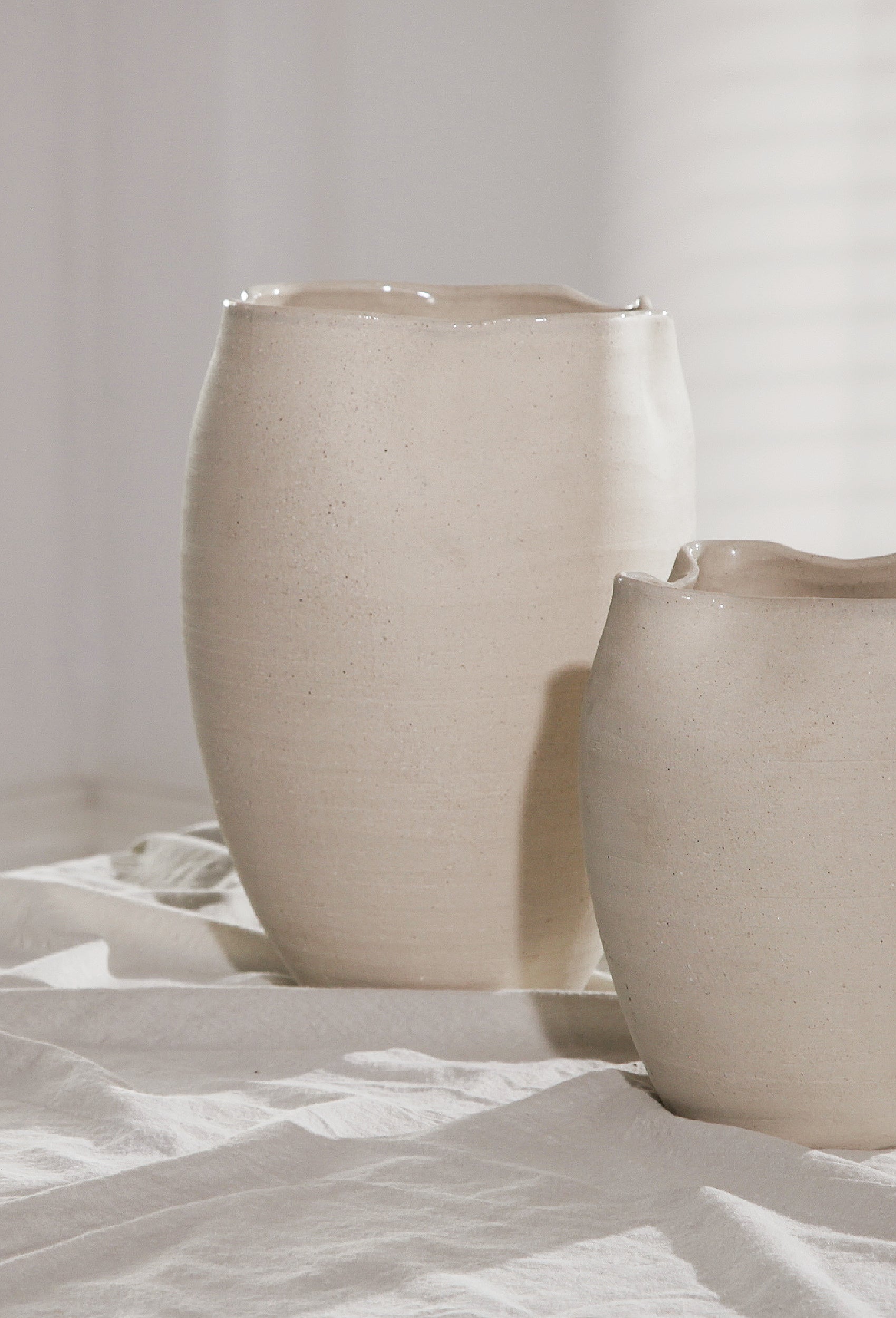 Two beige ceramic pots on a white surface with a light gray background